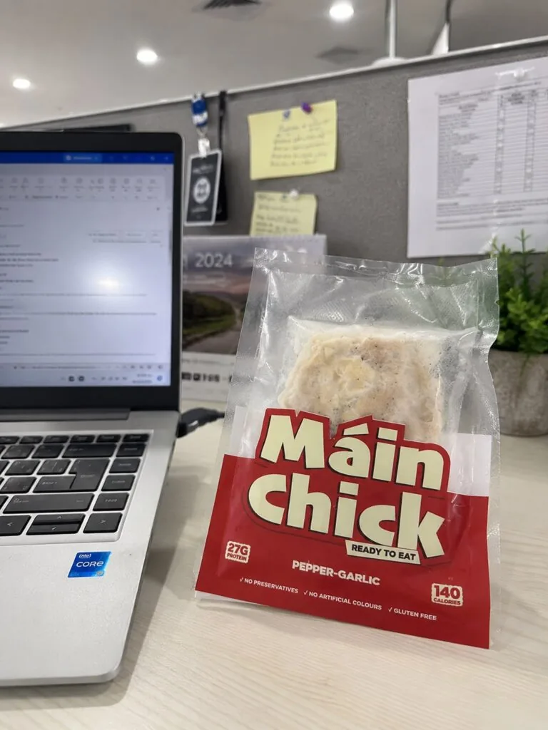 Máin Chick Pepper-Garlic pack on an office desk beside a laptop